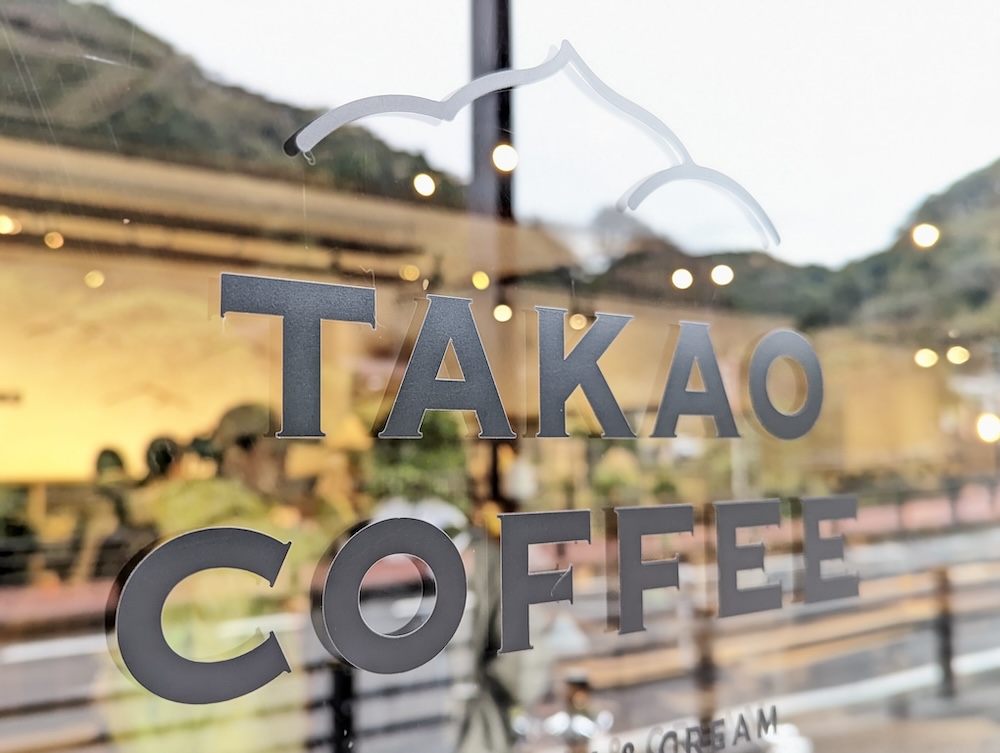 東京都八王子市の高尾山口駅から歩いて5分弱の場所に位置するカフェ「タカオコーヒー（TAKAO COFFEE ROASTERY & CREAM）」高尾山本店。山に囲まれた緑豊かな土地で、こだわりのコーヒーや季節限定ケーキ、日替わりケーキ、焼き菓子、その他スイーツを提供している。